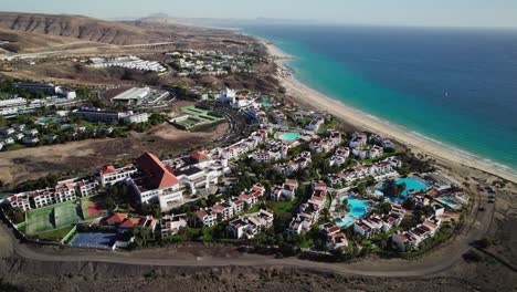Coastal-resort-in-Fuerteventura-with-hotels,-pools,-and-the-ocean,-aerial-view