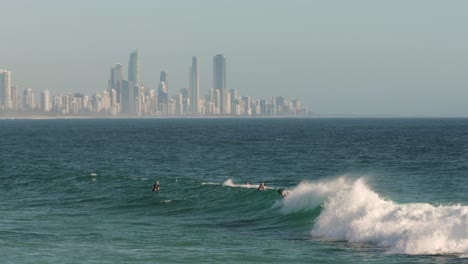 View-of-surfers-enjoying-the-waves-on-a-sunny-day-with-Surfers-Paradise-in-the-background,-Burleigh-Heads,-Gold-Coast,-Australia