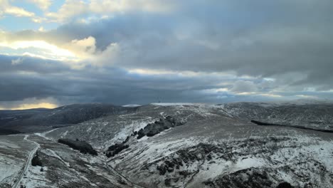Verschneite-Berglandschaft-Mit-Wolken-Und-Durchscheinendem-Sonnenlicht,-Luftaufnahme