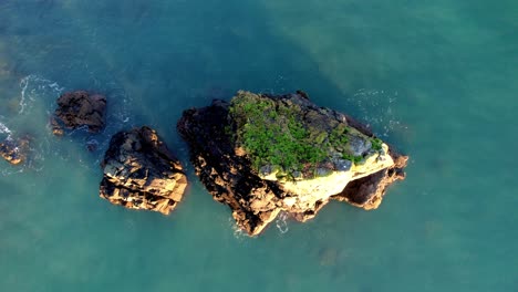 Drone-flying-up-from-small-island-revealing-pebble-beach-and-cliffs