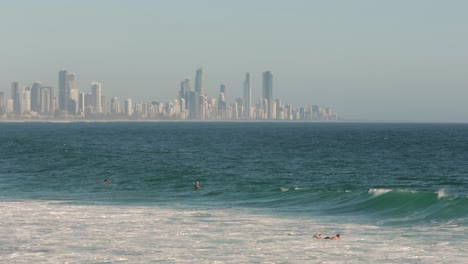 Surfers-waiting-for-waves-on-a-sunny-day-with-Surfers-Paradise-in-the-background,-Burleigh-Heads,-Gold-Coast,-Australia