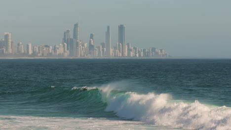 View-of-surfers-enjoying-the-waves-on-a-sunny-day-with-Surfers-Paradise-in-the-background,-Burleigh-Heads,-Gold-Coast,-Australia