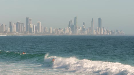 Surfer-paddling-onto-a-wave-with-Surfers-Paradise-in-the-background-on-a-sunny-day,-Burleigh-Heads,-Gold-Coast,-Australia