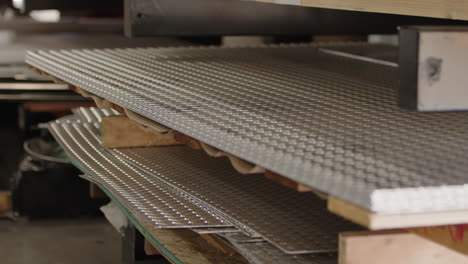 Close-up-of-stacked-metal-sheets-with-perforations-in-a-workshop,-shallow-depth-of-field