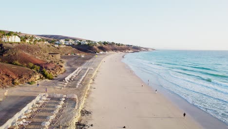 Costa-Arenosa-De-Fuerteventura-Con-Olas-Que-Se-Lavan-Suavemente,-Pocas-Personas-Esparcidas-Por-La-Playa,-Ambiente-Sereno,-Vista-Aérea