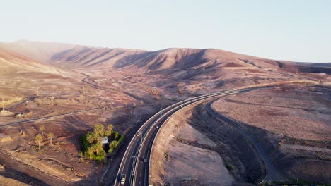 Winding-road-in-Fuerteventura's-arid-landscape,-early-morning-light,-aerial-view