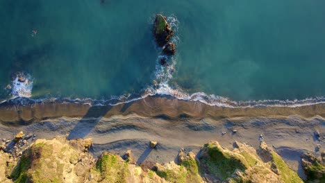 Drone-looking-down-on-pebble-beach-and-small-island-with-waves-Waterford-Ireland