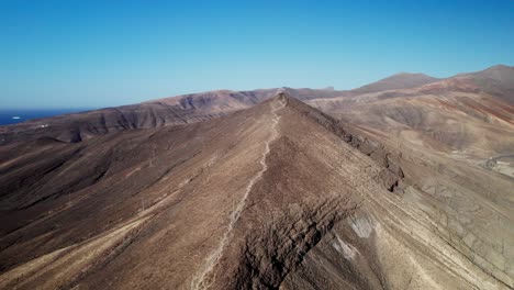 Arid,-undulating-landscape-of-Fuerteventura-with-mountains-and-clear-blue-sky,-aerial-view