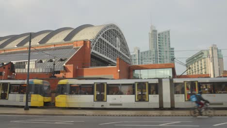 Panning-shot-of-Manchester-Central-Station-with-traffic-of-long-trams,-cars-and-cyclists