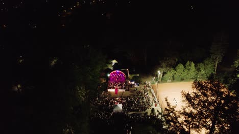 4k-Drone-Footage-of-Live-Music-Concert,-Illuminated-Stage-and-the-Crowd-in-the-Park-at-Nighttime