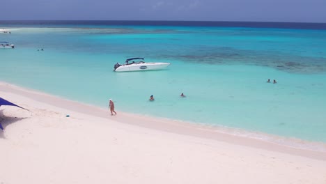 Pristine-beaches-and-turquoise-waters-of-Los-Roques,-Venezuela-with-boats-and-sunshades,-aerial-view