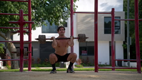 Slow-motion-of-a-shirtless-hispanic-man-performing-two-front-squats-at-the-fitness-area-of-a-local-park-in-Mexico