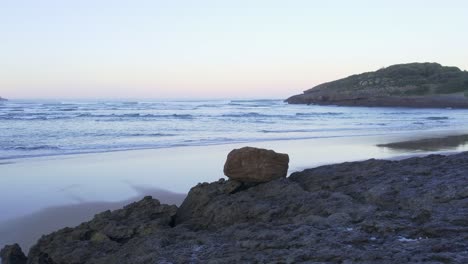 Low-4K-AERIAL-over-rocks-reveals-empty-idyllic-seascape-sunset-beach-Spain