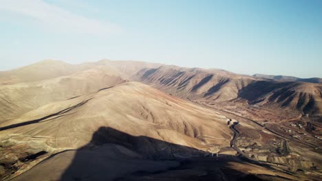 Arid-Fuerteventura-landscape,-dusty-roads-winding-through-barren-brown-hills,-clear-sky,-aerial-view