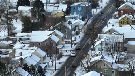 Long-aerial-zoom-of-cars-driving-on-road-through-USA-neighborhood-covered-in-winter-snow