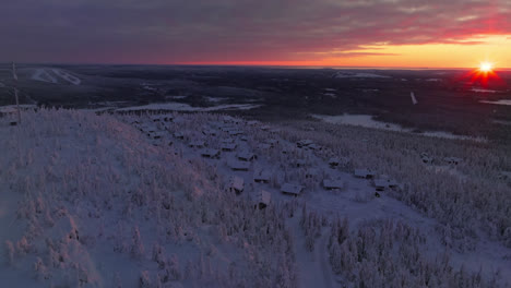 Aerial-tracking-shot-of-snowy-cabins-on-the-Iso-Syote-fell,-sunrise-in-Finland