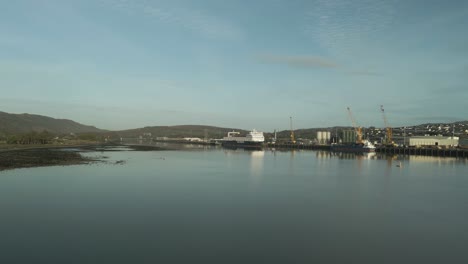 Calm-waters-reflecting-Omeath-town-and-port,-clear-sky,-hills-in-the-distance,-morning-light,-aerial-view