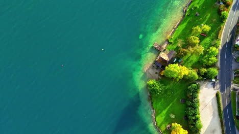 Aerial-of-lush-green-lakeside-with-crystal-clear-blue-water---Attersee,-Austria
