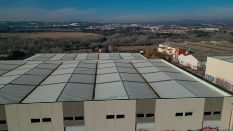 Large-industrial-warehouse-roof-with-the-landscape-of-Abrera,-Barcelona-in-the-background,-aerial-view