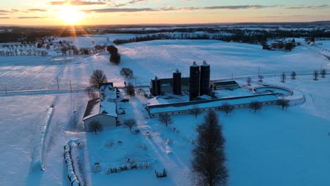 Aerial-reveal-of-sprawling-dairy-farm-in-winter-snow-during-sunset