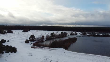 Aerial-rotating-view-over-belgian-lake-inside-forest-landscape-covered-in-snow,-winter-landscape