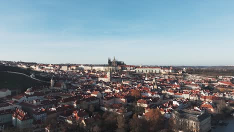 Slow-aerial-ascend-over-red-Prague-city-building-rooftops,-clear-sky-day