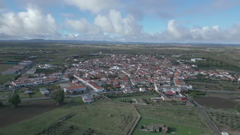 Añora,-showcasing-the-town's-layout-and-surrounding-landscapes-under-a-cloudy-sky,-aerial-view
