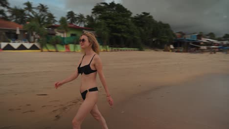 Beautiful-woman-walks-along-sandy-tropical-beach-in-black-bikini-enjoying-a-tropical-vacation
