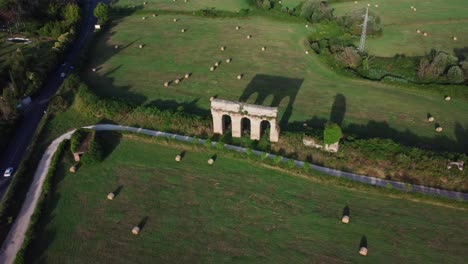 Ancient-Roman-aqueduct-in-Montalto,-Lazio,-Italy,-with-hay-bales-and-shadows-on-the-grass,-aerial-view