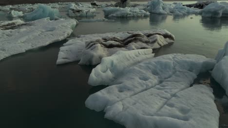Icebergs-Flotando-En-El-Lago-Glaciar-De-Islandia,-Revelación-Cinematográfica-De-Inclinación-Aérea