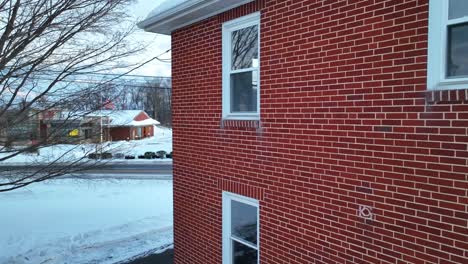 Aerial-push-in-on-rear-bedroom-window-of-two-story-brick-home-covered-in-winter-snow