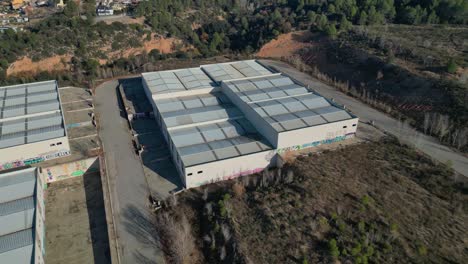 Industrial-warehouses-near-Abrera,-Barcelona,-Spain,-surrounded-by-trees,-aerial-view