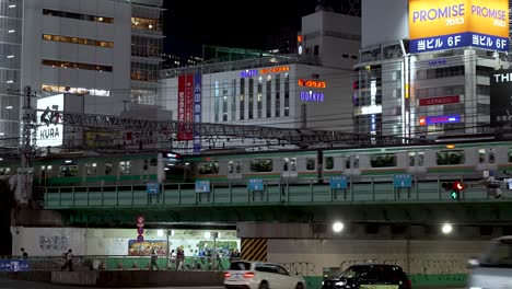 En-La-Vibrante-Metrópolis-De-Tokio,-Japón,-Un-Tren-De-La-Línea-Yamanote-Atraviesa-Rápidamente-Vías-Elevadas-En-El-Bullicioso-Distrito-De-Shinjuku.