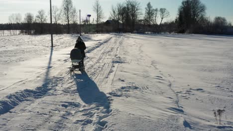Mother-remove-jacket-hood-while-walk-with-baby-carriage-on-snowy-winter-road