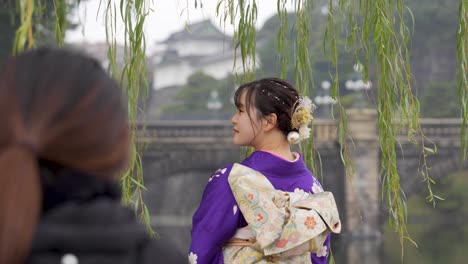 Woman-in-traditional-kimono-admiring-a-bridge-and-castle-across-the-river-in-Tokyo,-Japan,-overcast-day