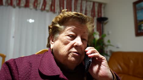 Elderly-woman-talking-on-a-phone-call-in-her-living-room