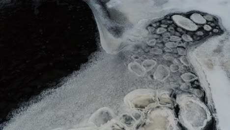 Frozen-ice-pieces-in-pattern-float-on-dark-pond-water-surface-near-ice-sheet