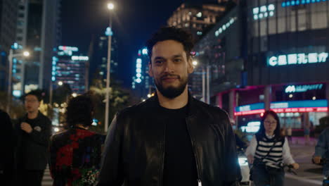 caucasian-male-standing-in-front-of-camera-at-night-with-pedestrian-walking-around-at-evening-in-smart-modern-city