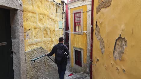 Stylish-male-traveler-explores-old-alleyway-stairs-with-yellow-paint-peeling-off-building,-Porto