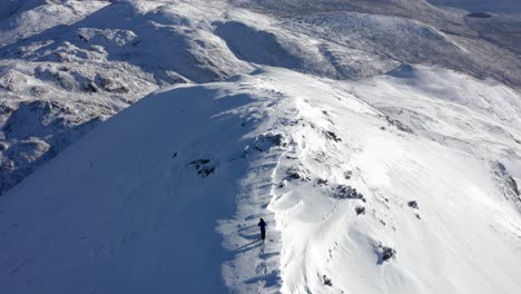 Solo-hiker-walking-on-snowy-peak-under-sunlight