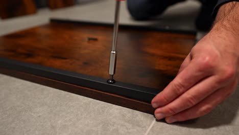 Male-hand-screwing-a-screw-in-a-wooden-table-to-assemble-kitchen-furniture