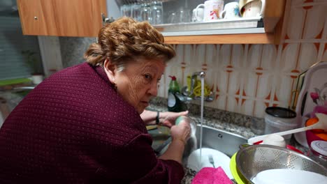 Old-woman-washing-dishes-while-the-tap-is-opened-loosing-water