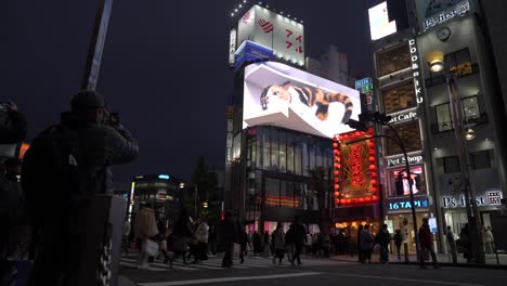 3D-cat-billboard-at-Shinjuku-Station,-Japan,-with-pedestrians-and-a-photographer,-evening-view
