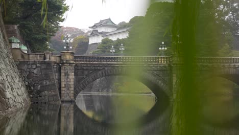 Imperial-Palace-bridge-with-reflection-on-water-in-Tokyo,-Japan,-overcast-sky,-weeping-willow-tree-in-foreground