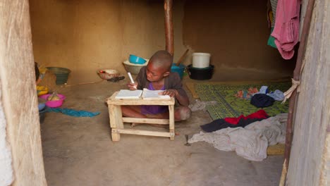 Front-view-of-a-dedicated-young-boy-studying-on-the-daylight-in-his-traditional-mud-house-in-Wulugu-village,-Ghana