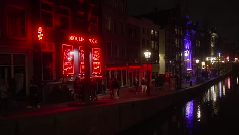 Gente-Caminando-Por-El-Barrio-Rojo-De-Ámsterdam-Con-Coloridos-Bares-Para-Adultos-Con-Carteles-De-Neón