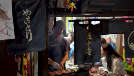 Belebter-Japanischer-Street-Food-Stand-Mit-Einem-Koch,-Der-Mahlzeiten-Zubereitet,-Im-Hintergrund-Gäste