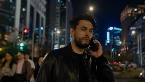 caucasian-male-talking-at-phone-modern-smartphone-in-urban-cityscape-illuminated-at-night-with-people-and-car-traffic