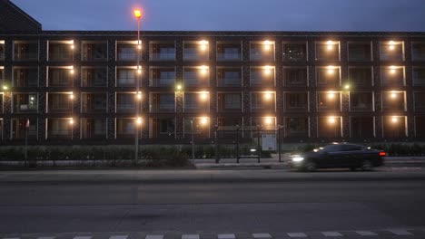 Edificio-Arquitectónico-Moderno-En-Amsterdam-Con-Automóviles-Circulando-Por-La-Carretera-Con-Parada-De-Autobús-Vacía-Durante-La-Hora-Azul