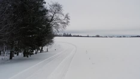 Small-snowy-countryside-road-with-car-tire-tracks-near-tree-and-river